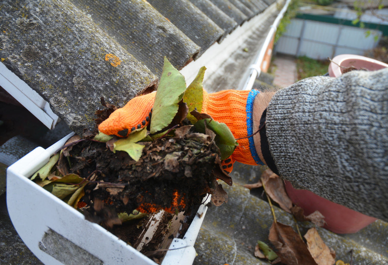 A person wearing orange gloves is cleaning a gutter on a roof.