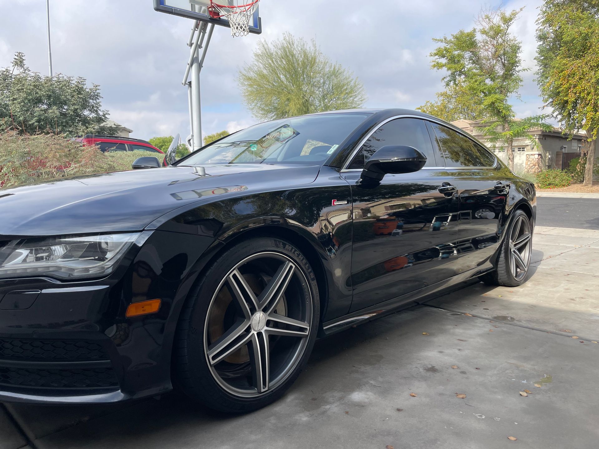 Black Audi A7 with custom wheels parked on a driveway in front of a basketball hoop.
