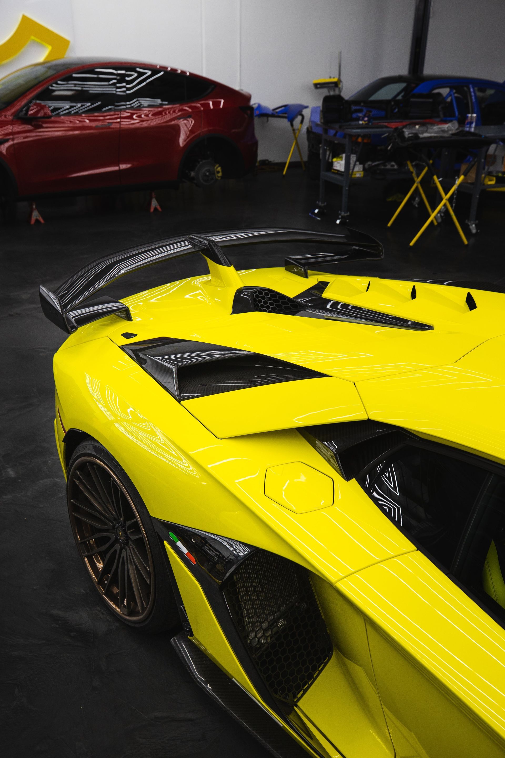 Yellow Lamborghini with carbon fiber accents inside a garage; other cars in the background.