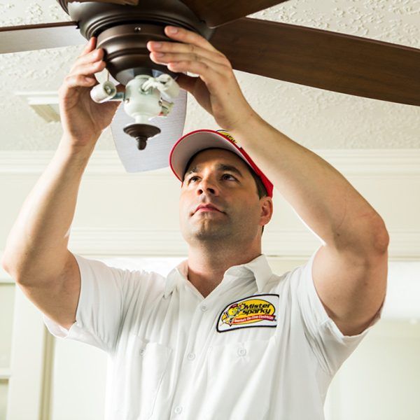 A man is fixing a ceiling fan in a room