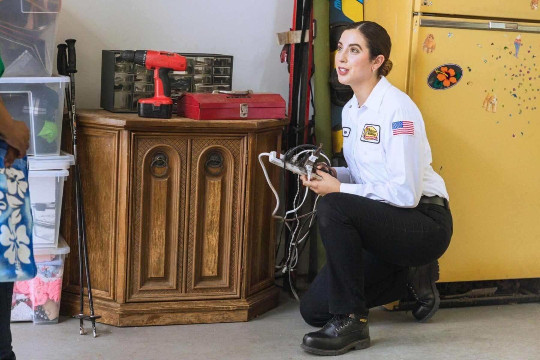 A woman is kneeling down in a garage holding a cord.