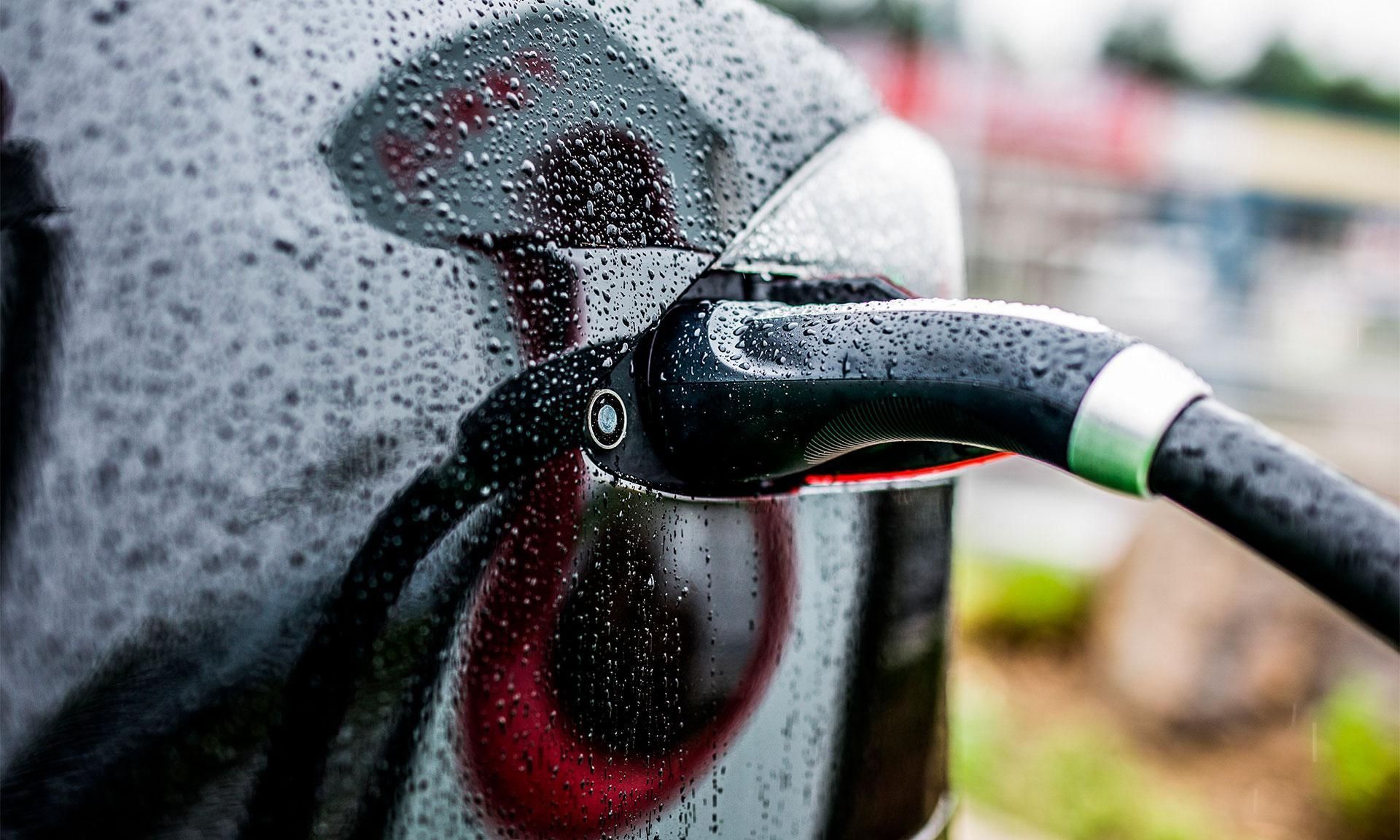 An electric car is being charged at a charging station in the rain.