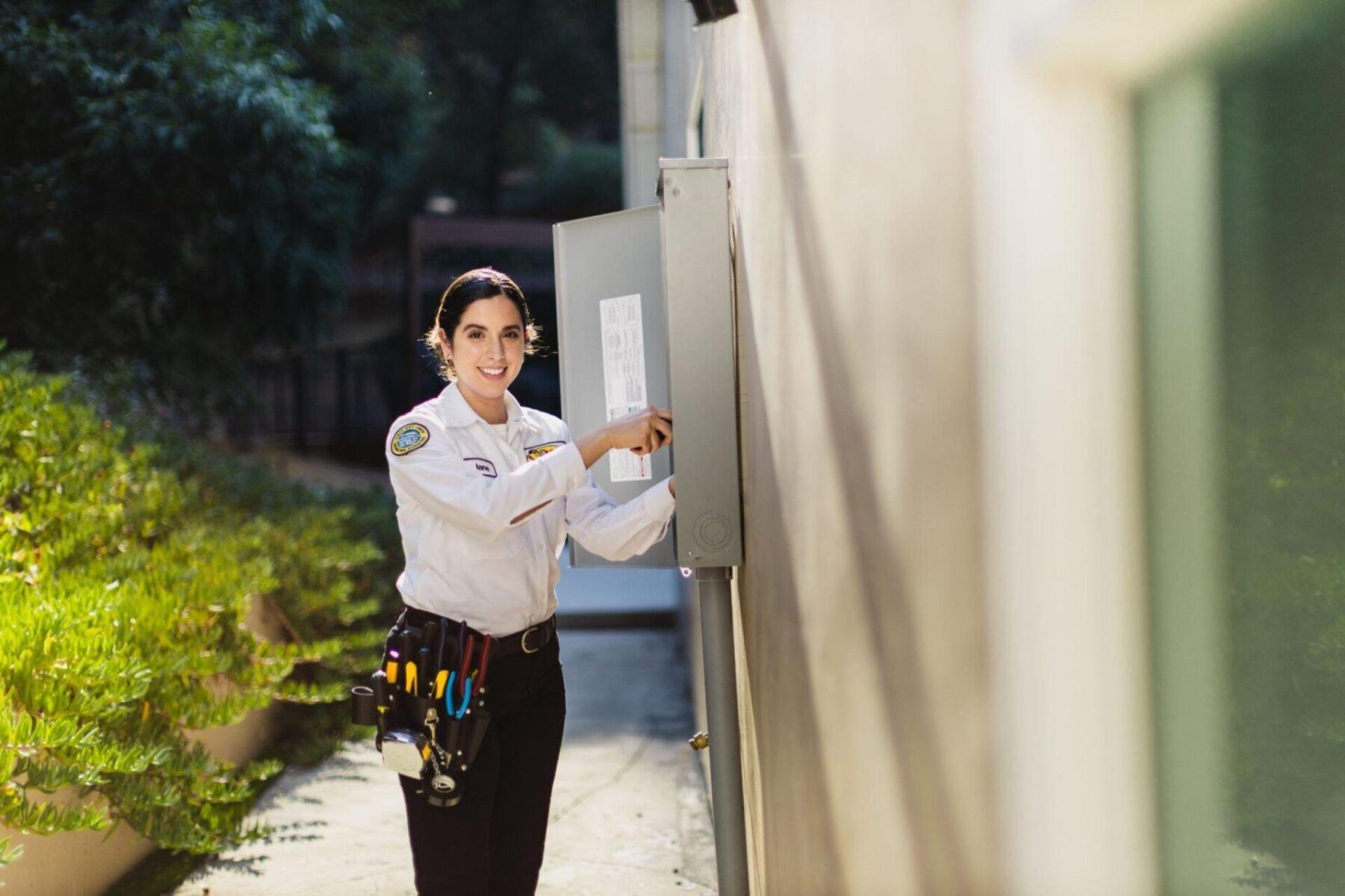 A woman in a Mister Sparky shirt and black pants is standing next to a wall.