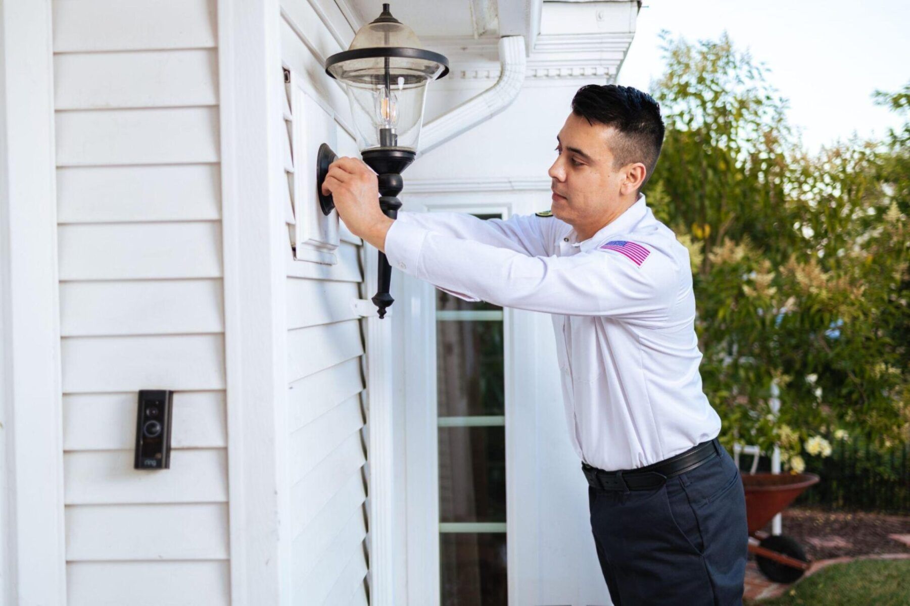 A man is fixing a light on the side of a house.