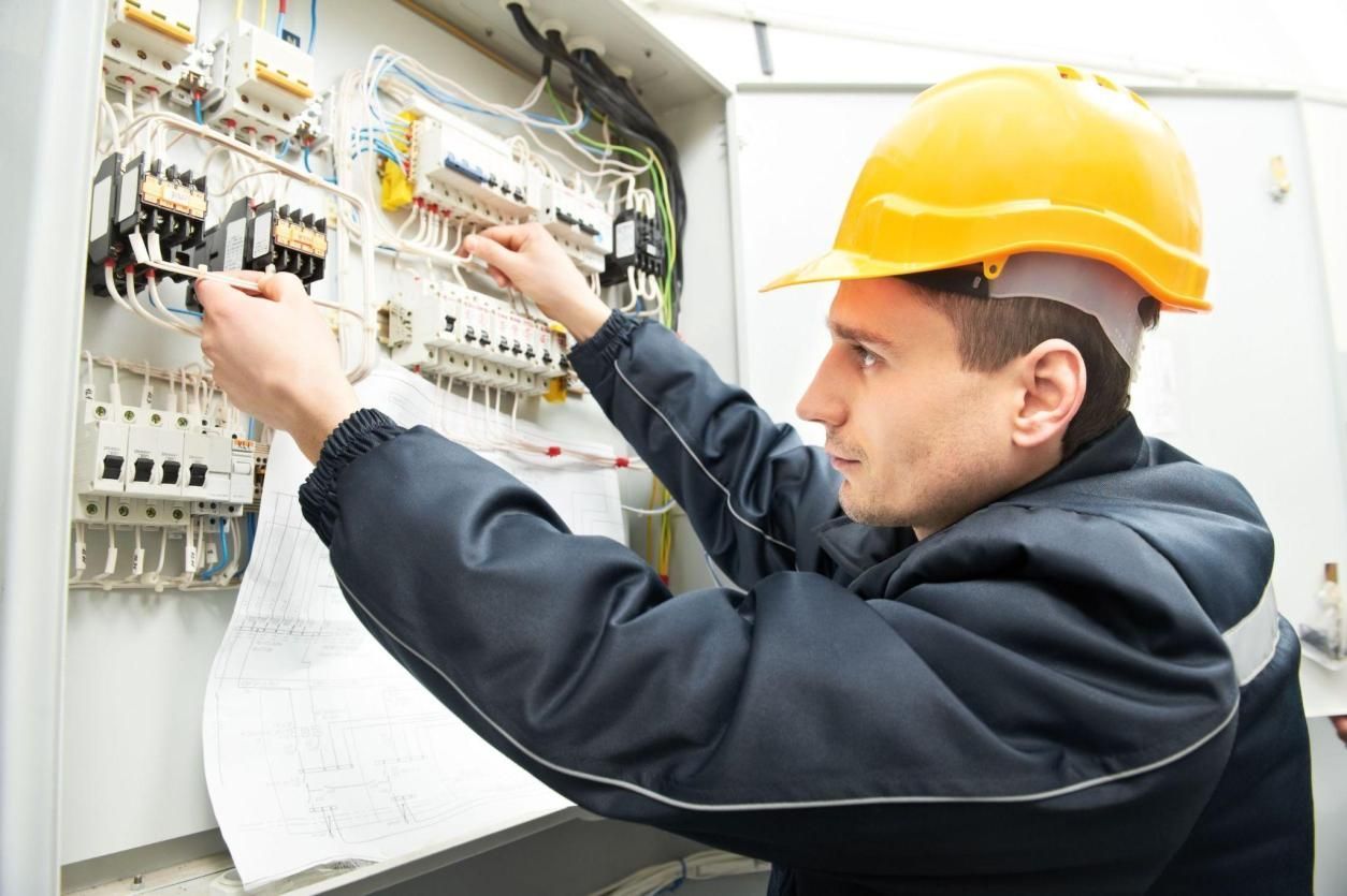 A man wearing a hard hat is working on an electrical box.