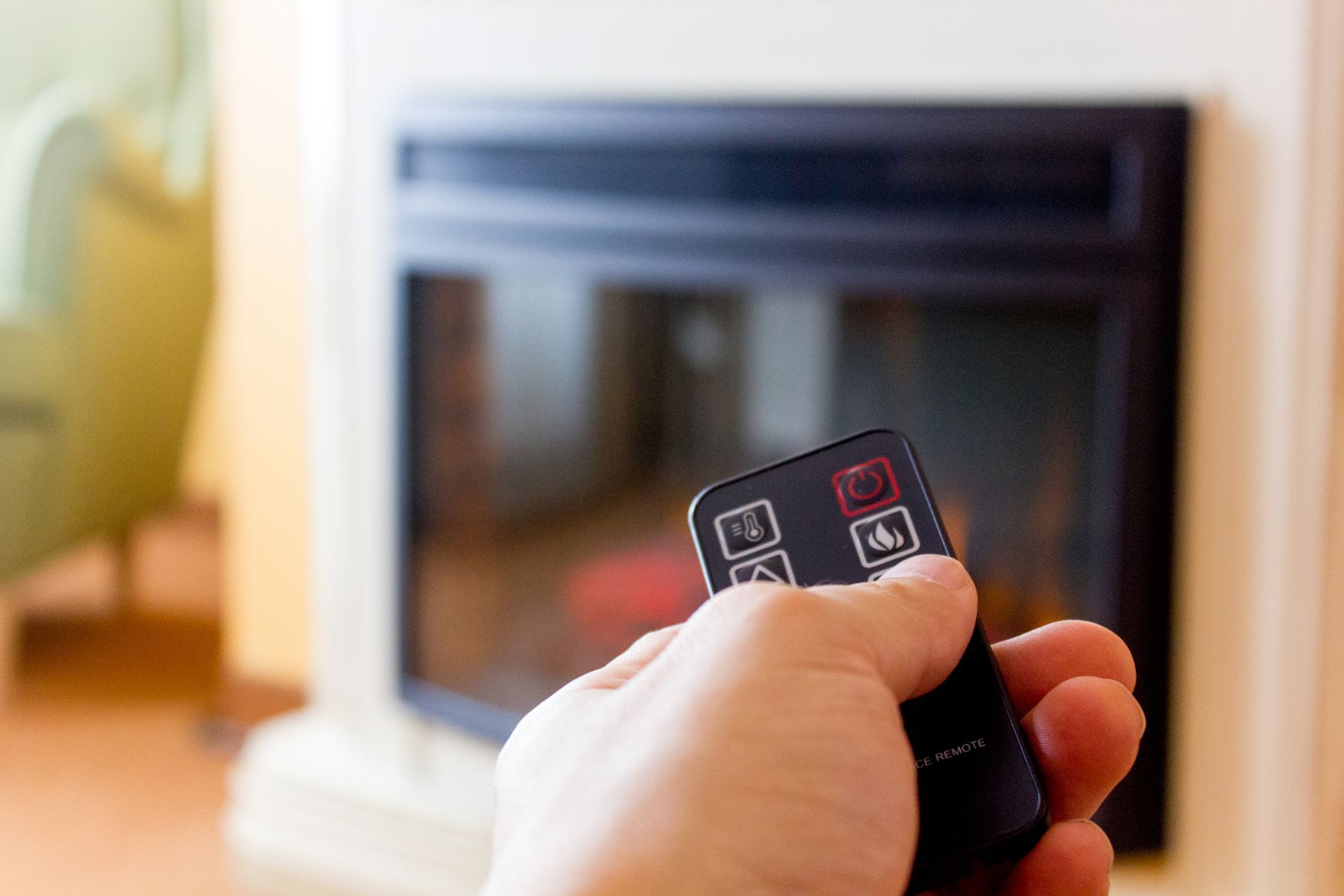 A person is holding a remote control in front of an electric fireplace.