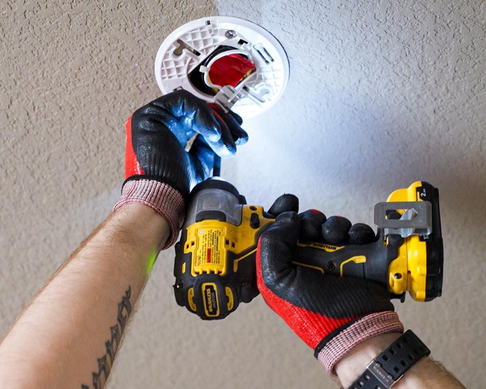 Mister Sparky gloved hands install smoke detector