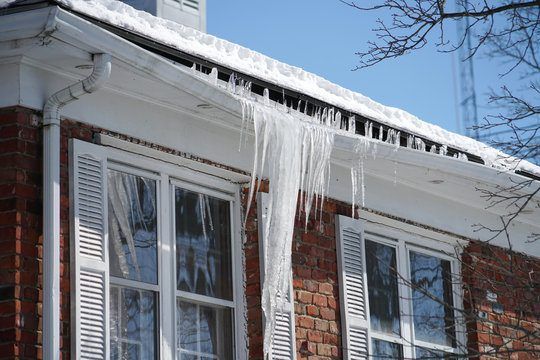 Icicles are hanging from the roof of a brick house.