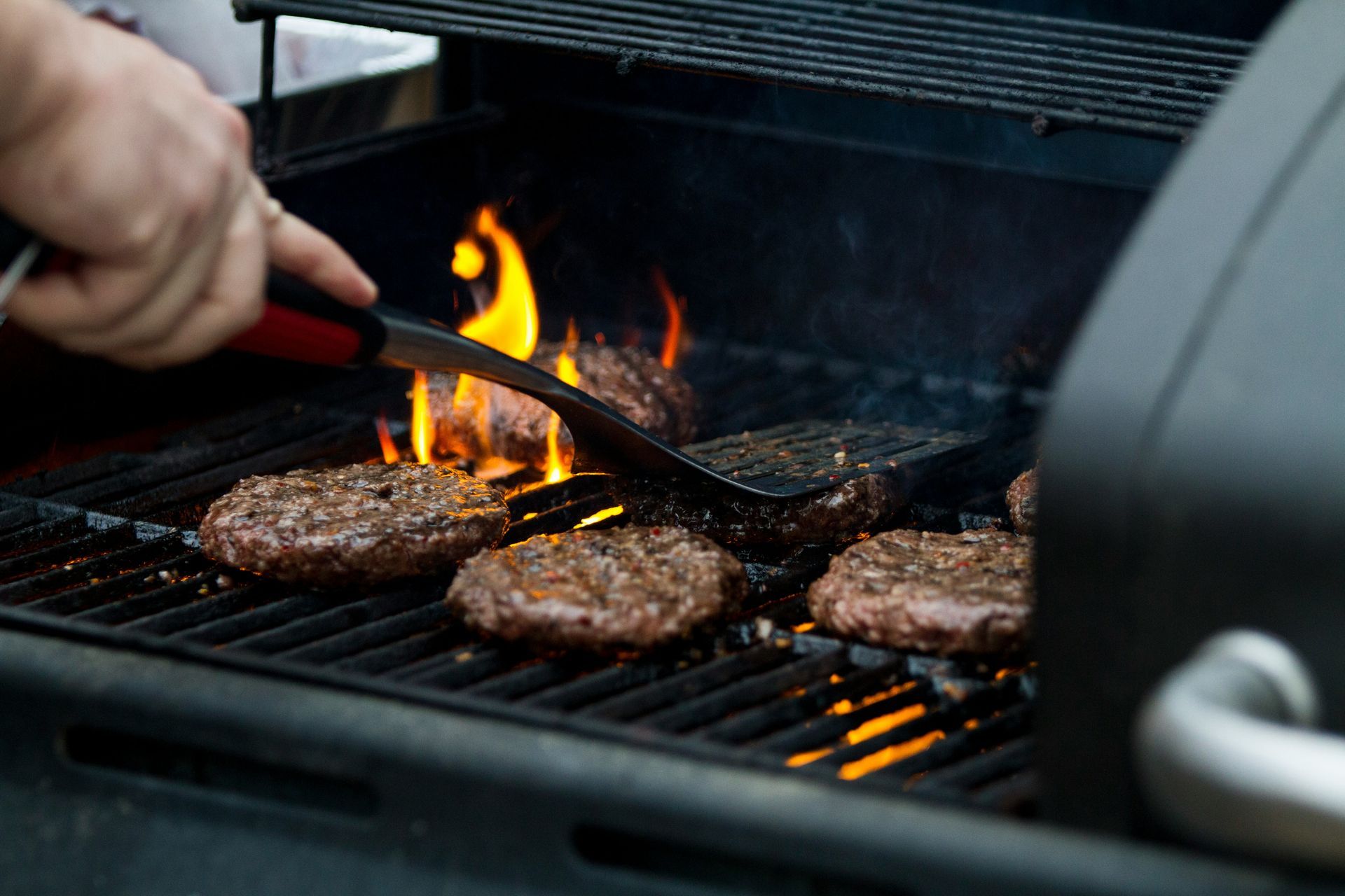 A person is cooking hamburgers on a grill.