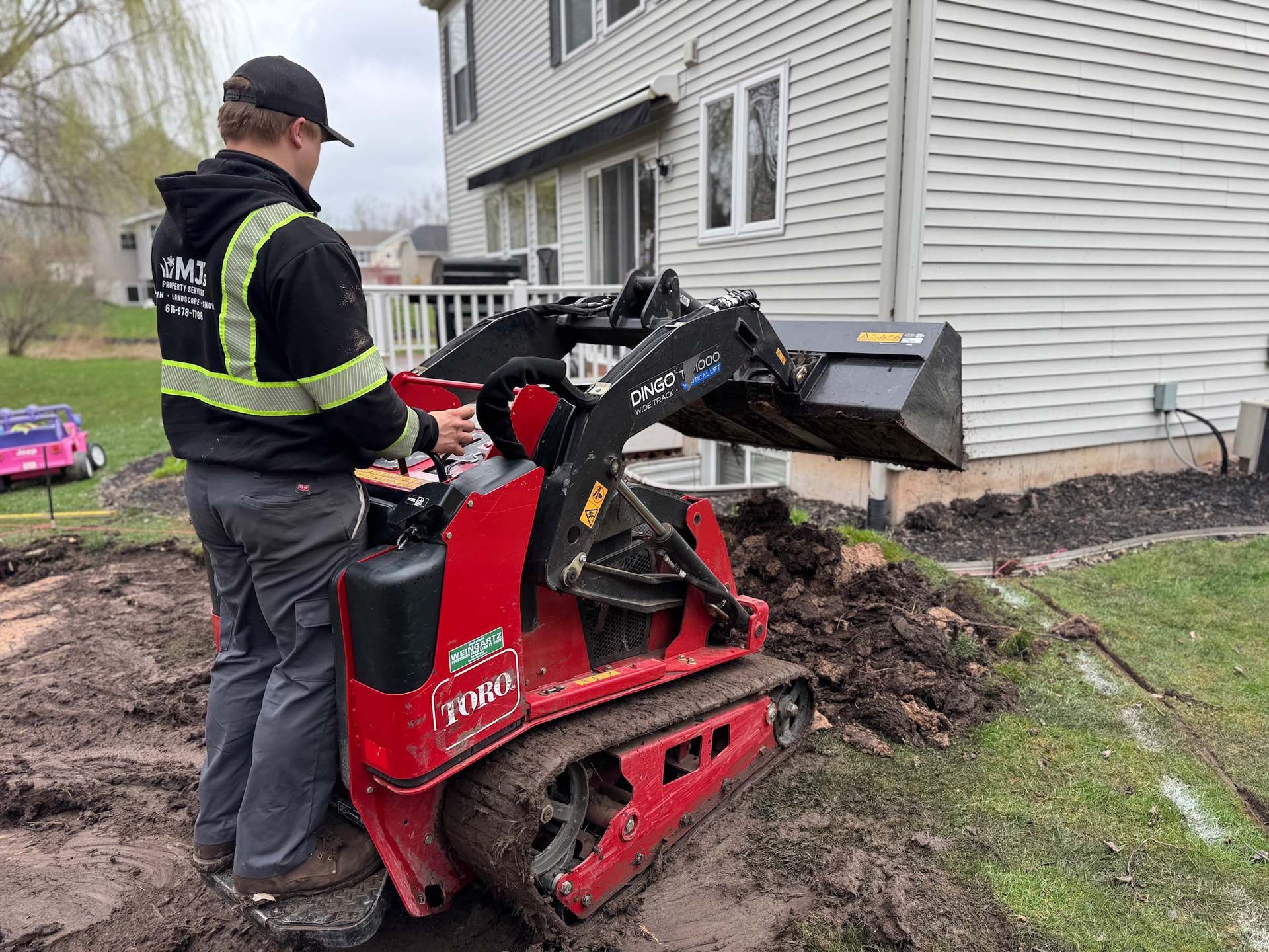 A man is standing next to a small red tractor in front of a house.