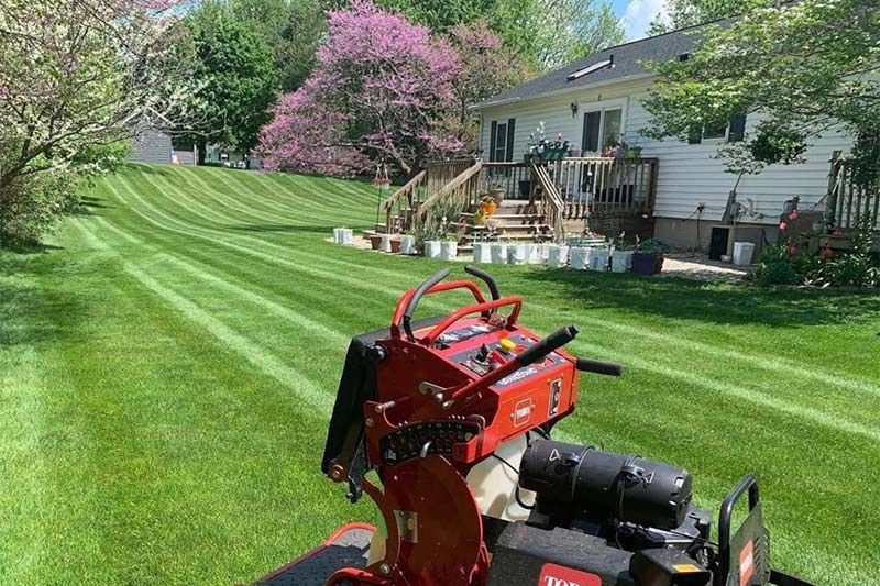 A lawn mower is sitting on top of a lush green lawn in front of a house.