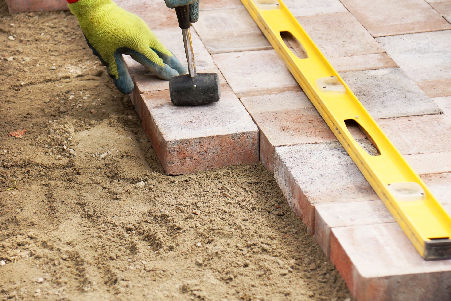 A person is laying bricks on the ground with a hammer and a level.