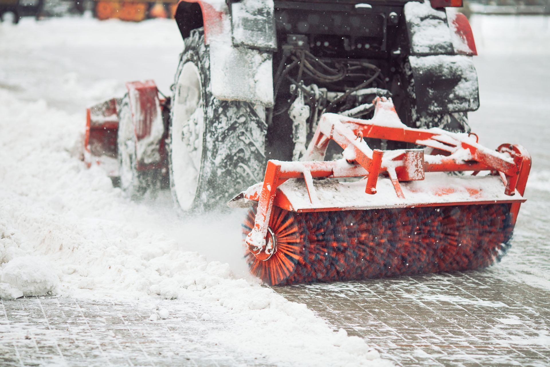 A tractor is clearing snow from the road with a broom.
