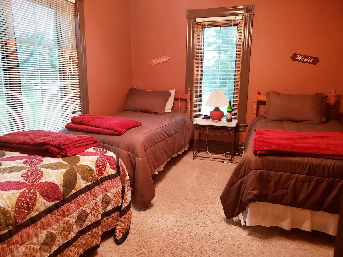 A bedroom with three twin beds covered in brown and red bedding. The walls are painted orange.