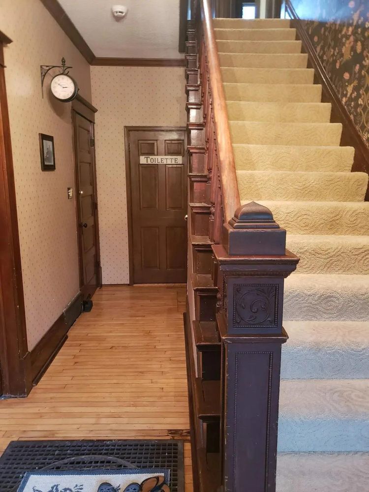 A wooden staircase and hallway. The stairs have a light carpet, a dark wooden banister, and lead upwards.