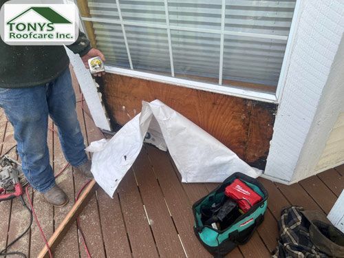 A man is standing on a deck holding a tape measure next to a window.