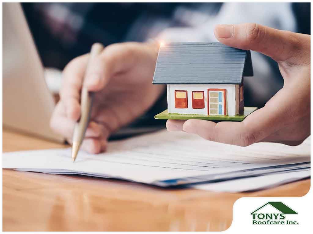 A person is writing on a piece of paper while holding a small model house.