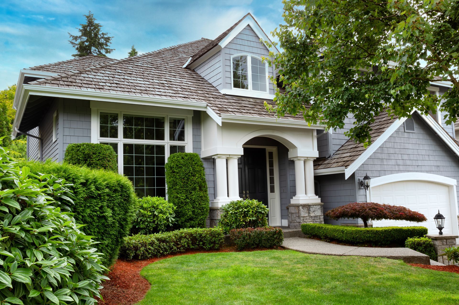A large gray house with a large lawn in front of it with a beautiful roof