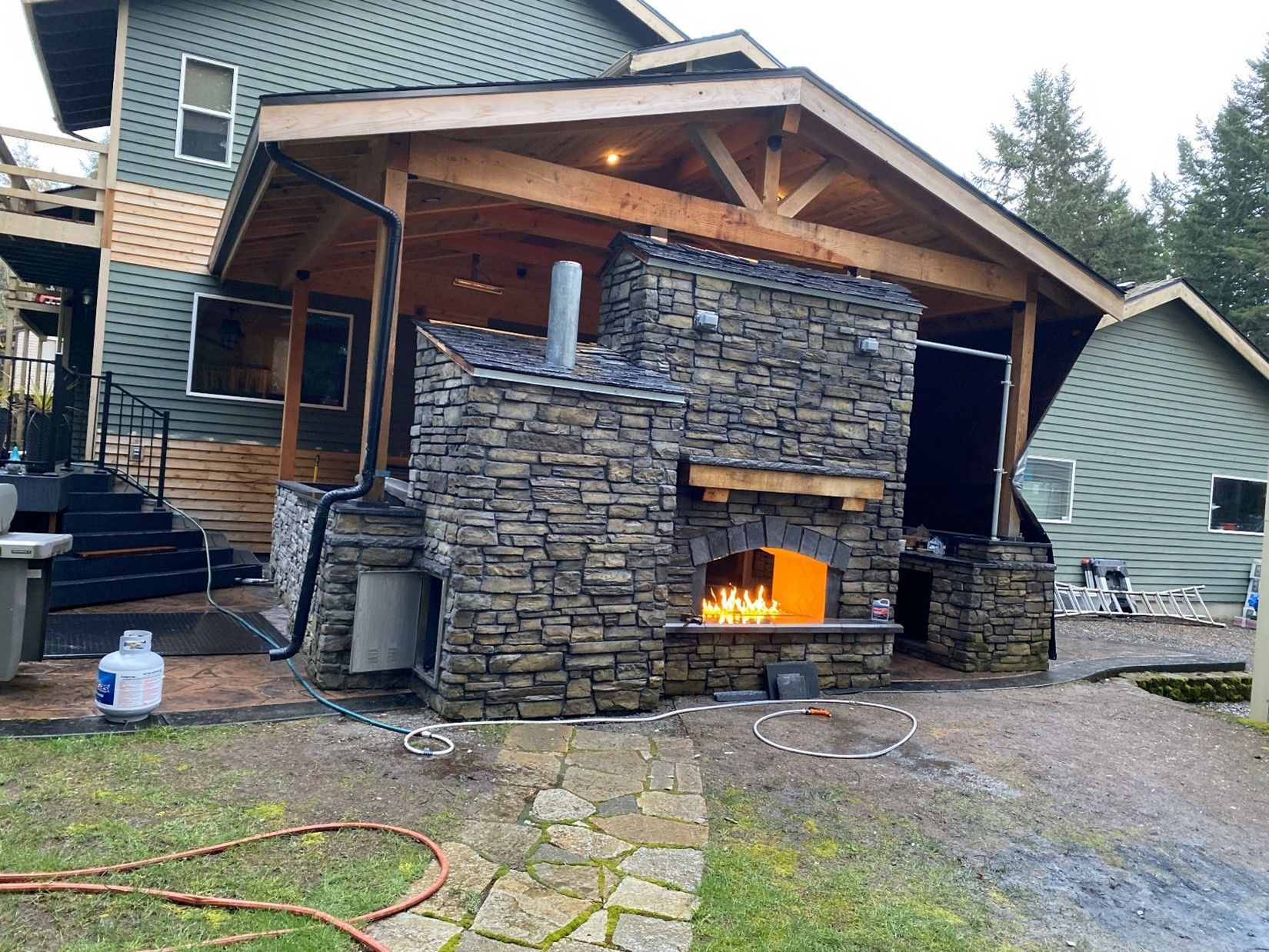 A house with an outdoor stone fireplace kitchen and custom roof cover for the patio in front of it