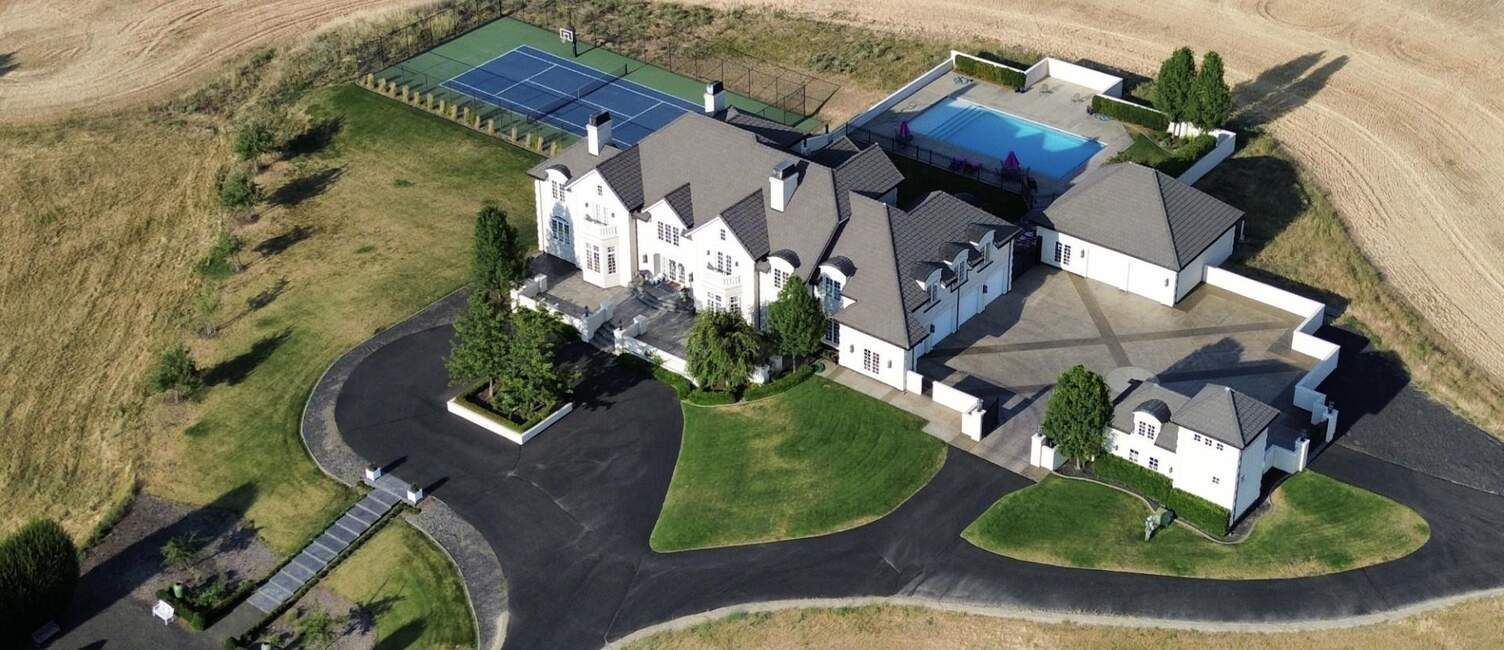 An aerial view of a large house with a tennis court and pool