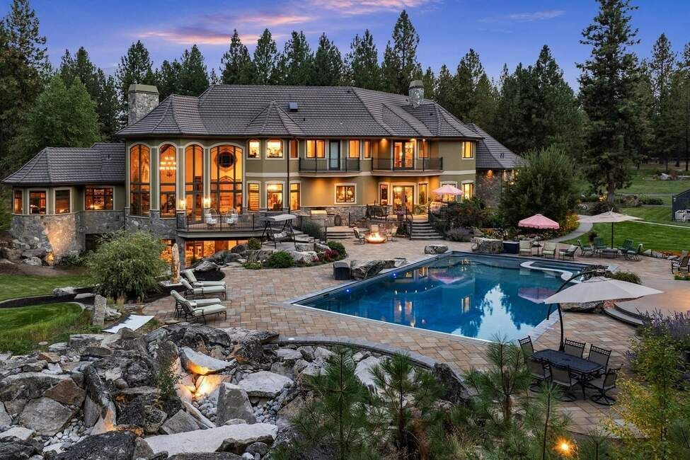 A large house with a large swimming pool in front of it surrounded by trees in Spokane.