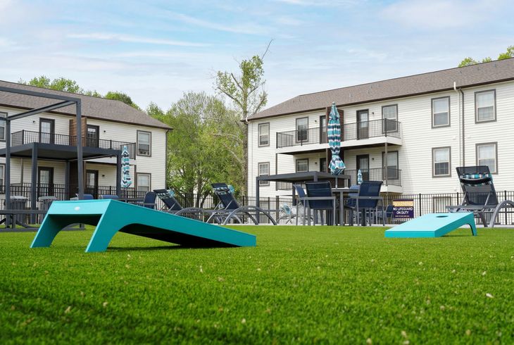 Pool area with turquoise water, lounge chairs, and a two-story apartment building.