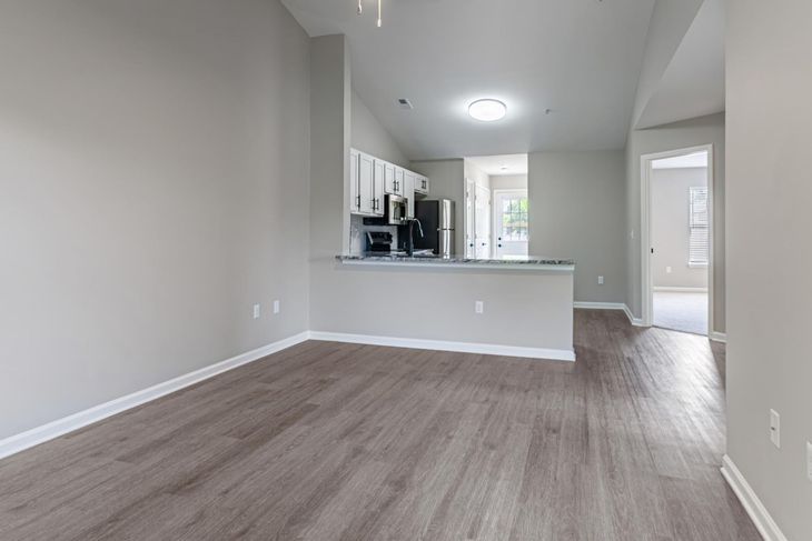 Empty apartment with gray walls, dark wood floors, and a kitchen area.