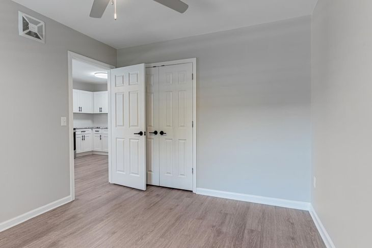 Empty apartment with gray walls, dark wood floors, and a kitchen area.