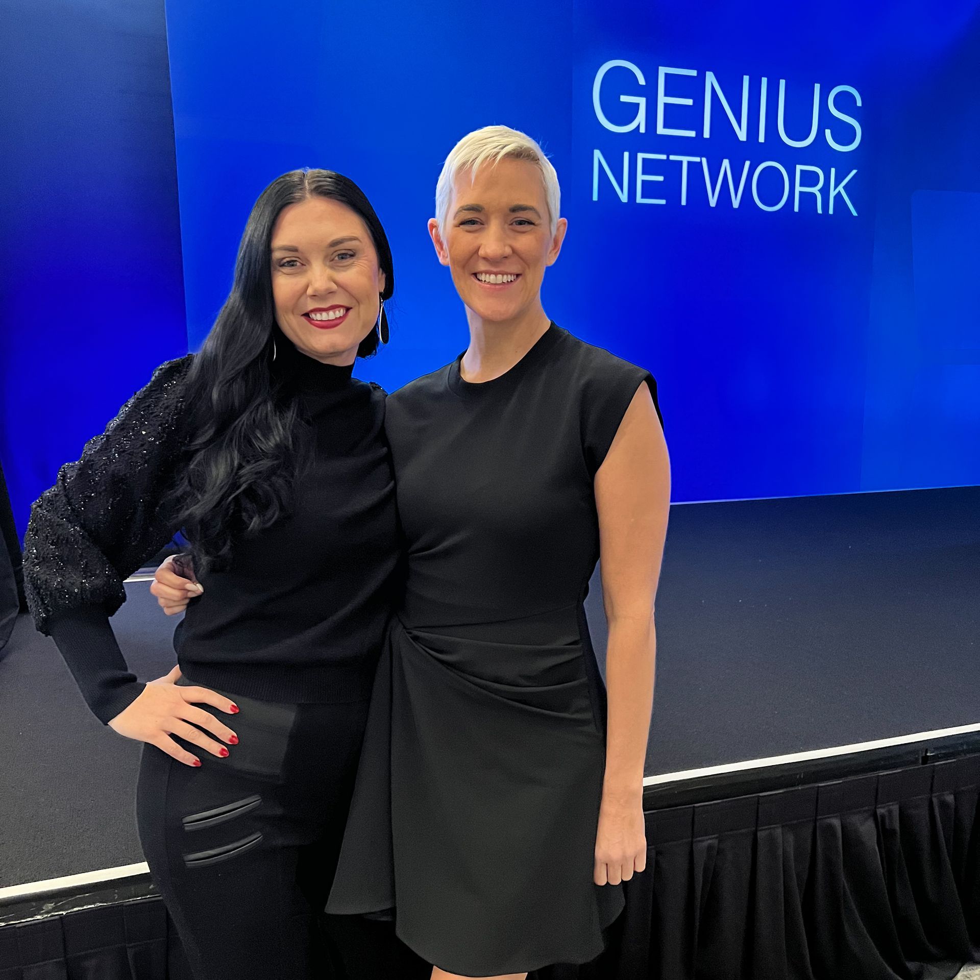 Two women are posing for a picture in front of a sign that says genius network