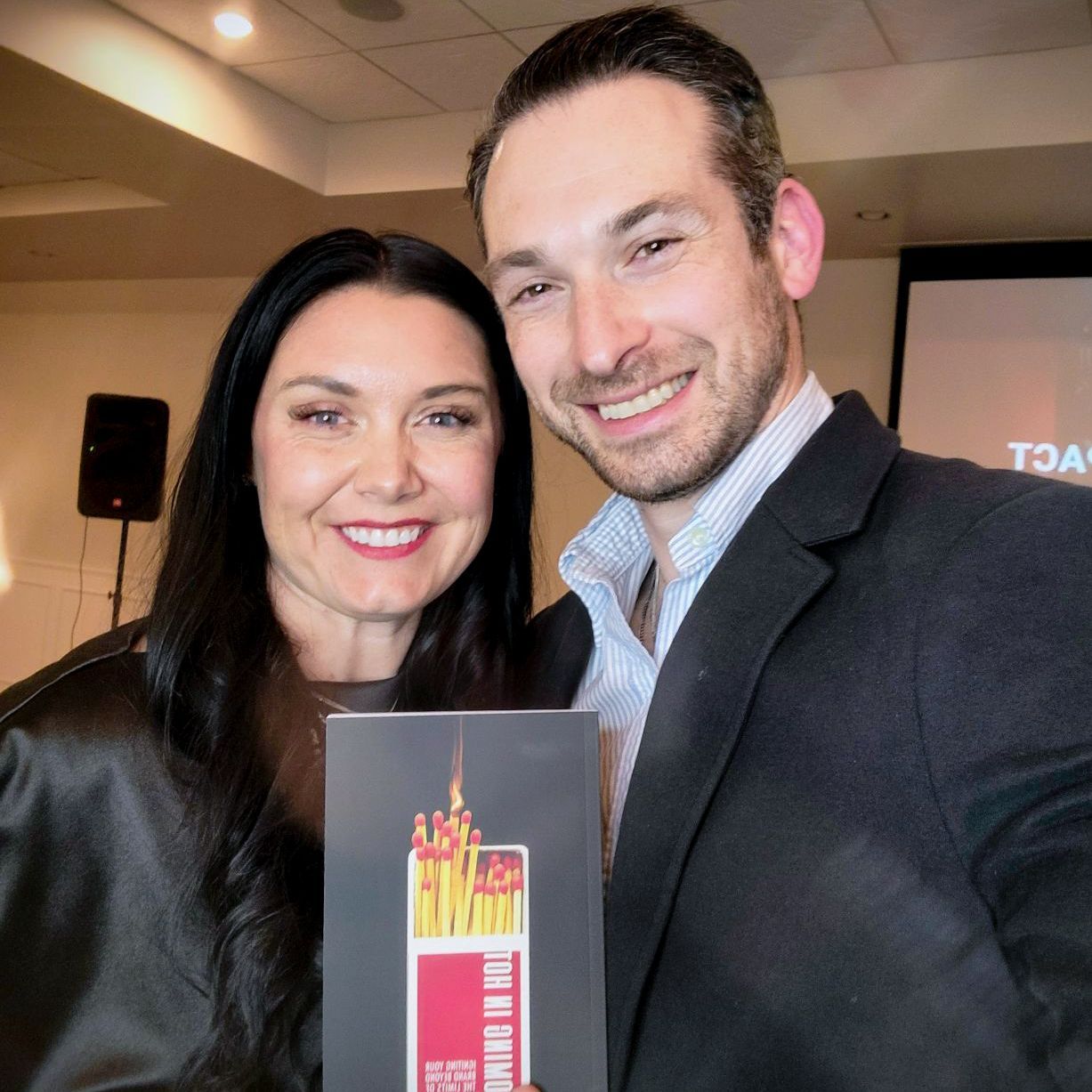 A man and a woman are posing for a picture and the man is holding a book that says ' fire ' on it
