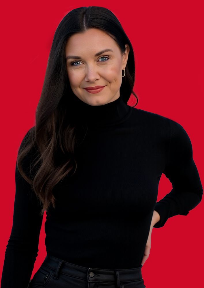 A woman wearing a black turtleneck sweater and black jeans is standing in front of a red background.