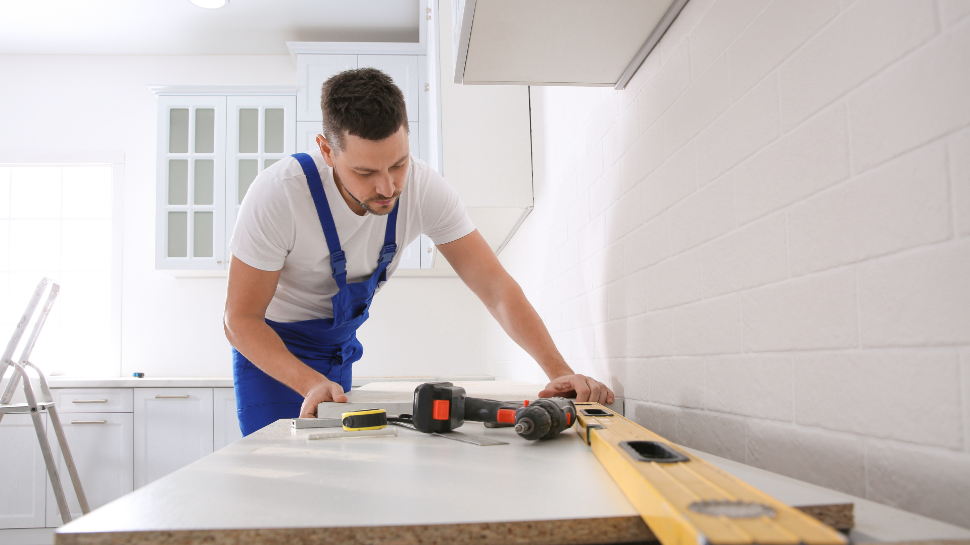 A man is working on a kitchen counter with a drill and a level.