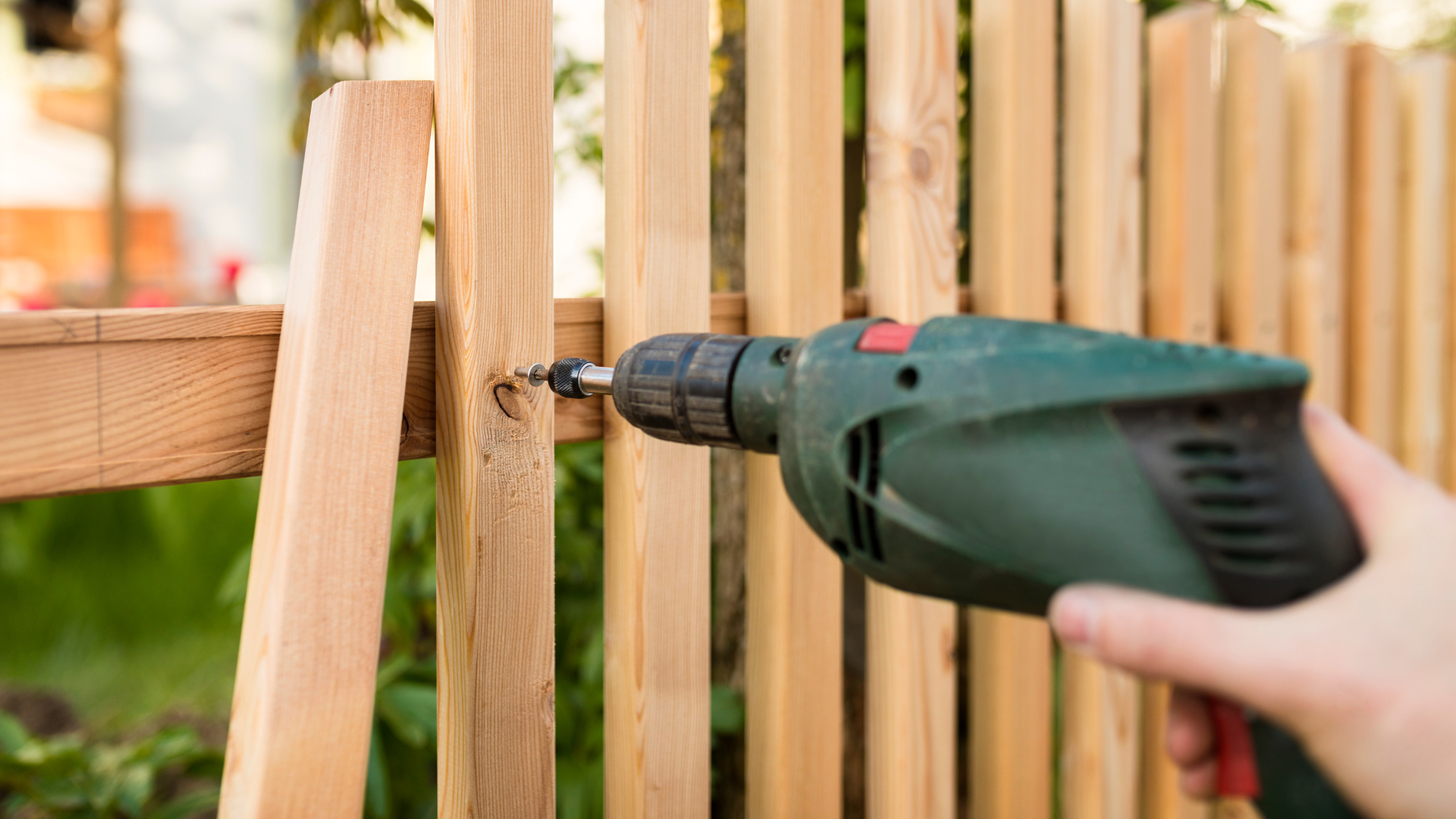 A person is drilling a hole in a wooden fence with a drill.