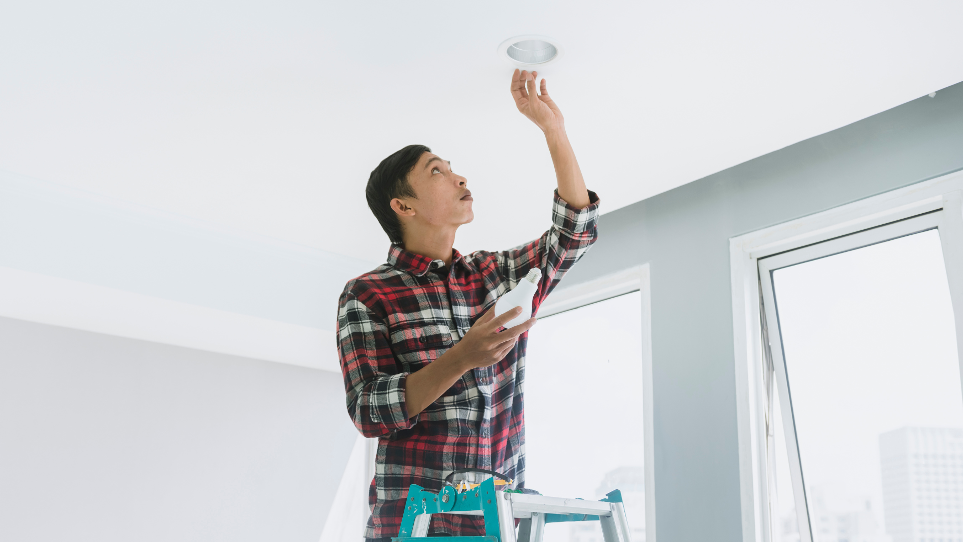 A man is standing on a ladder fixing a light fixture.
