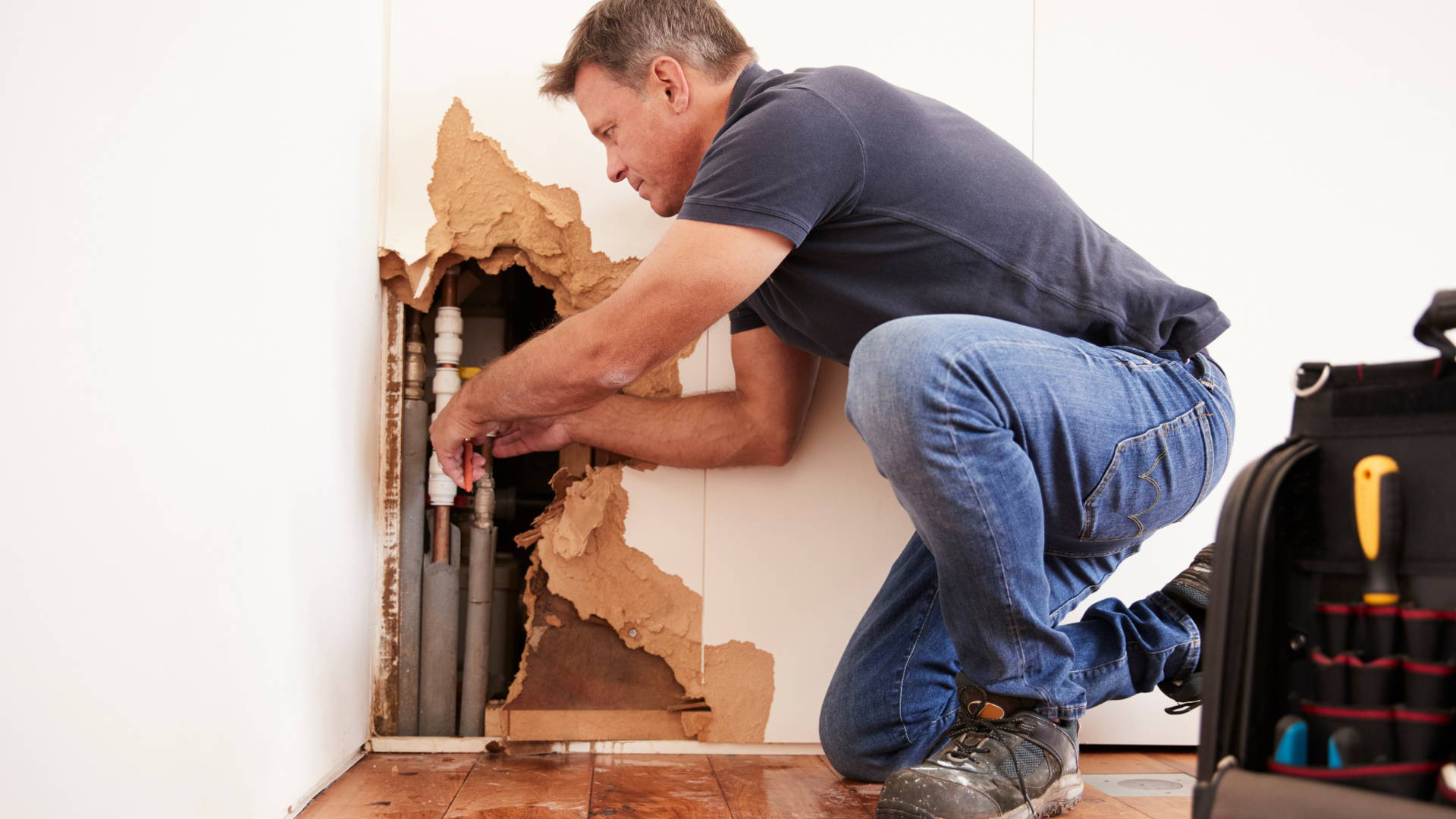 A man is kneeling down in a room fixing a pipe.