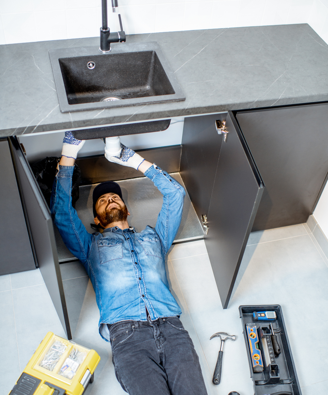 A man is laying on the floor under a kitchen sink.