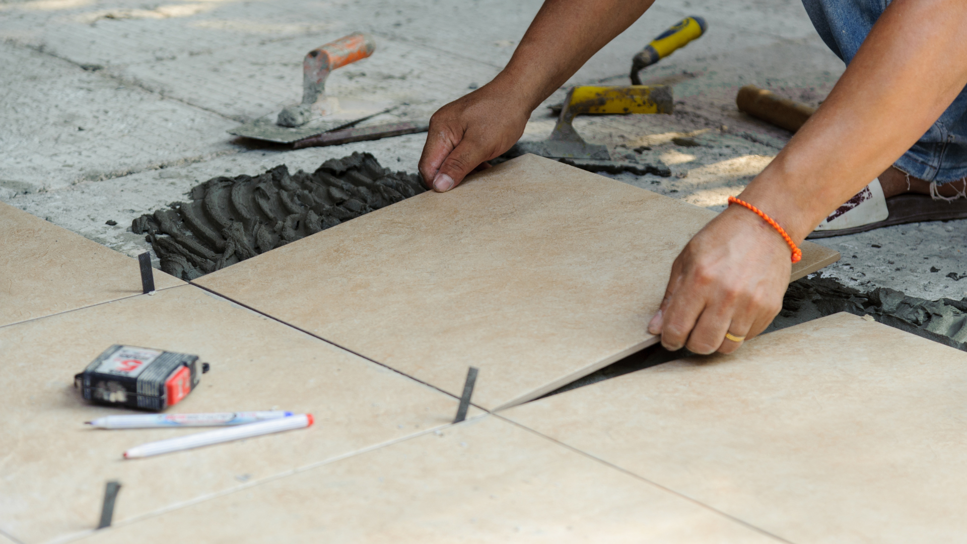 A person is laying tiles on a concrete floor.