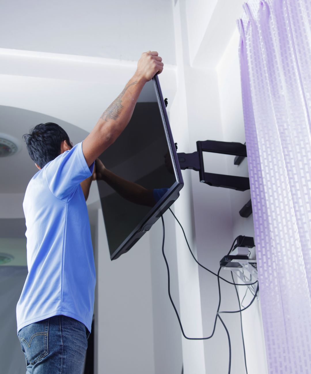 A man in a blue shirt is installing a flat screen tv