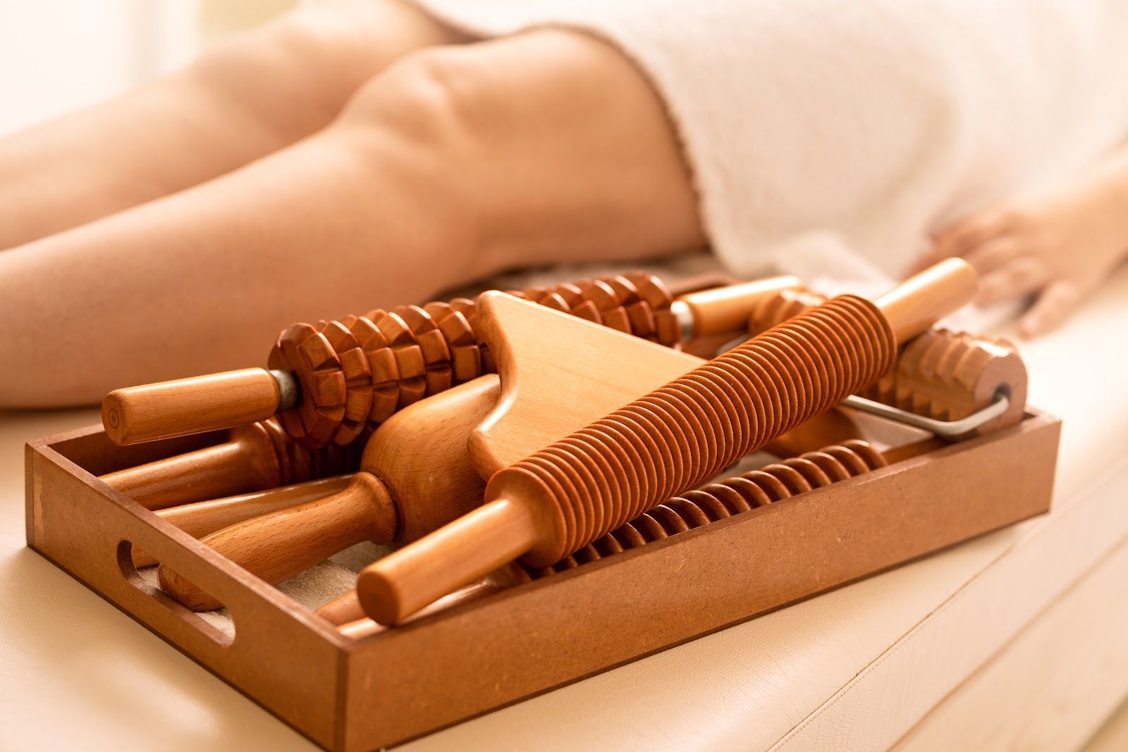 Wooden massage tools in a tray on a massage table with a leg in the background.
