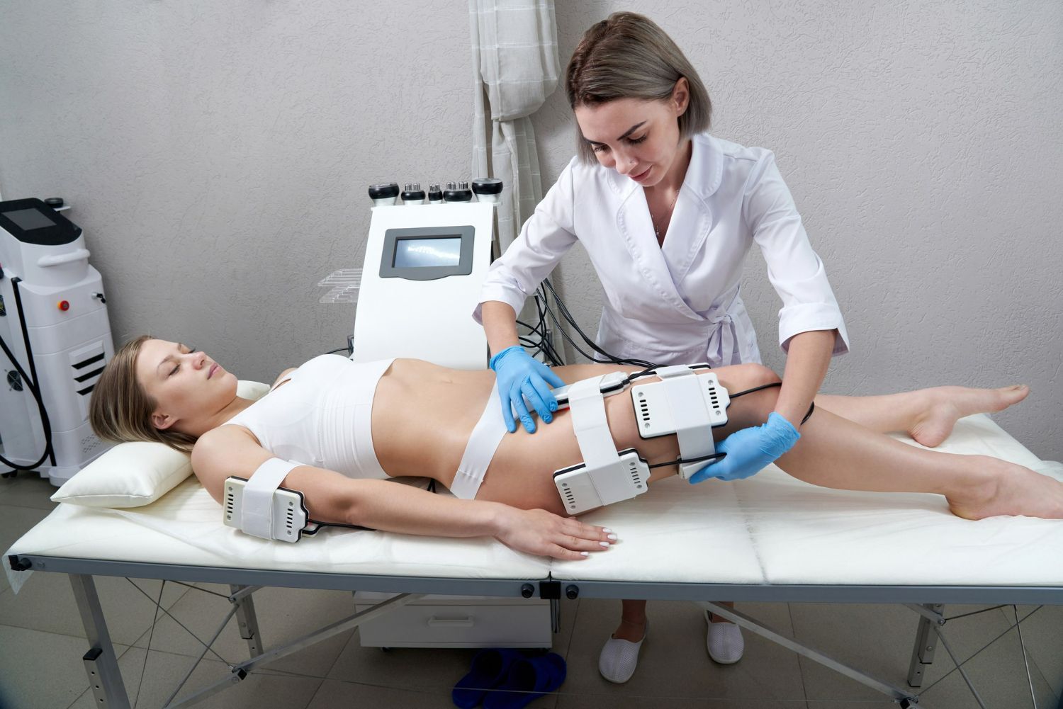 A woman receives body contouring treatment from a technician in a clinic.