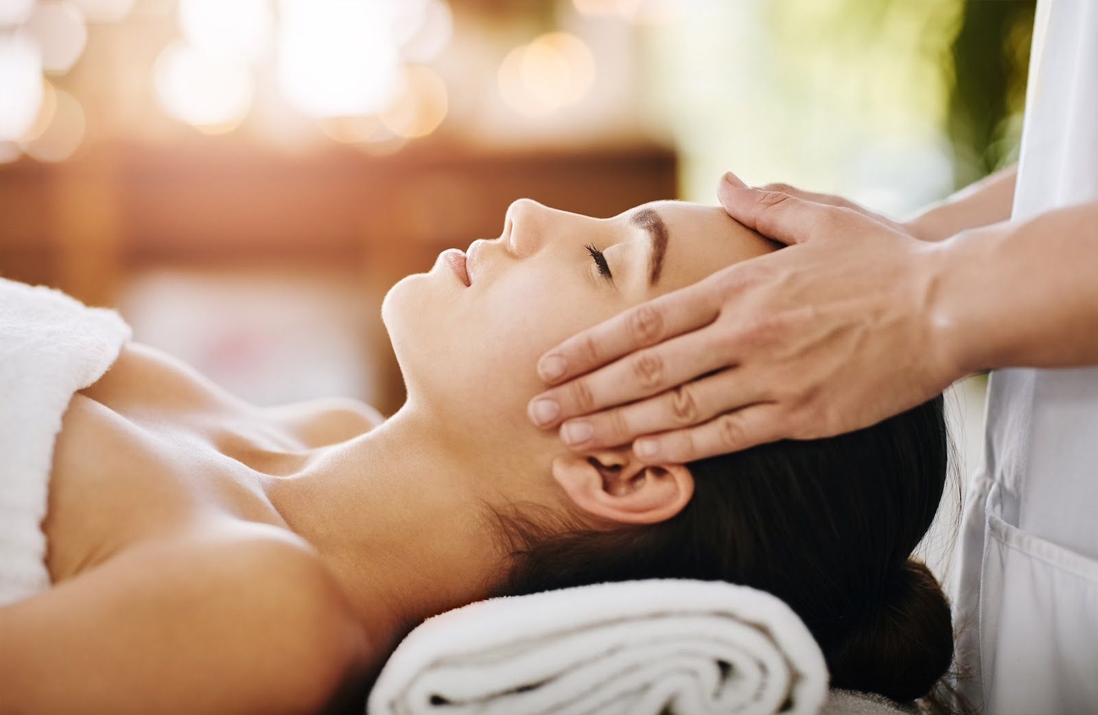 Woman receiving a facial massage at a spa; hands on her forehead, eyes closed.