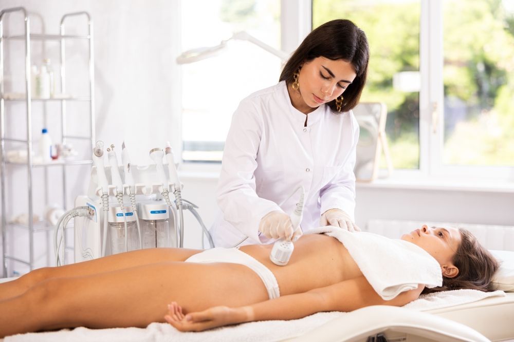A woman in a white coat performs a procedure on a patient's torso. Setting: medical office.