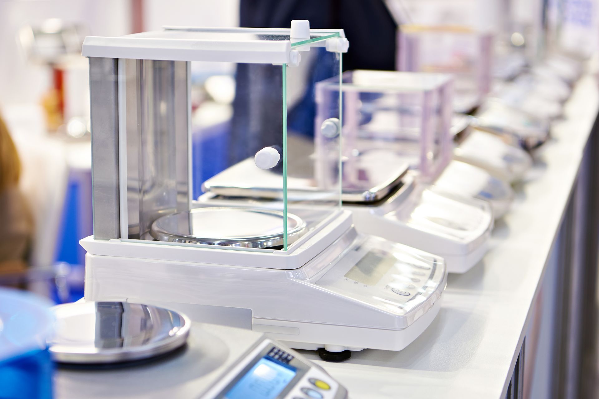 Laboratory scales lined up on a countertop, with glass enclosures protecting the weighing plates.