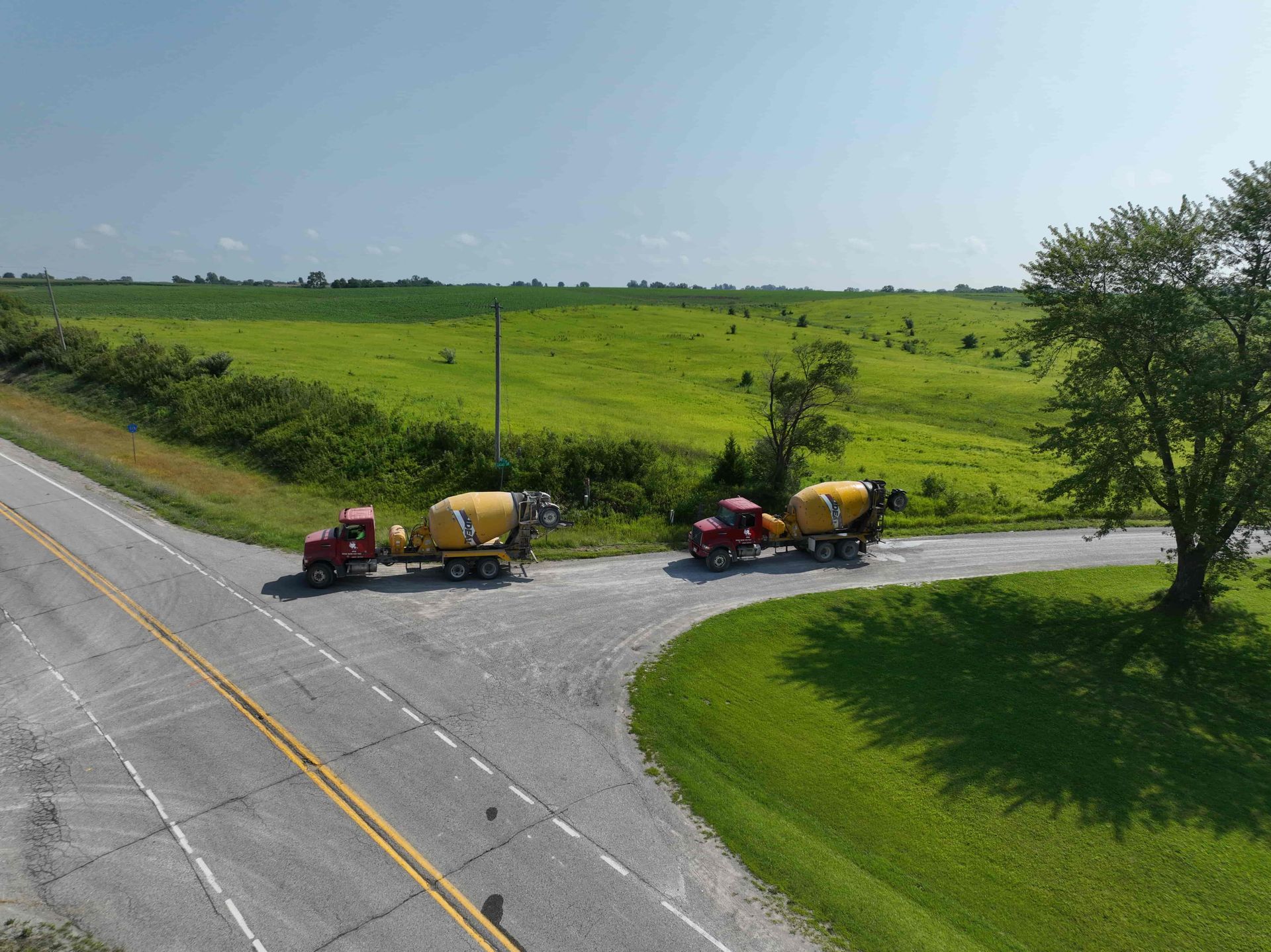 A couple of trucks are driving down a road next to a field.