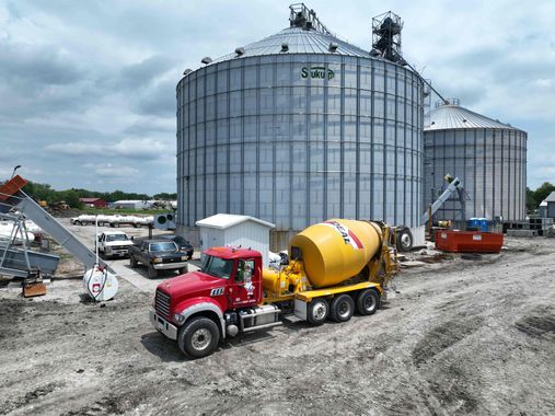 A red truck is driving down a dirt road in front of two silos.