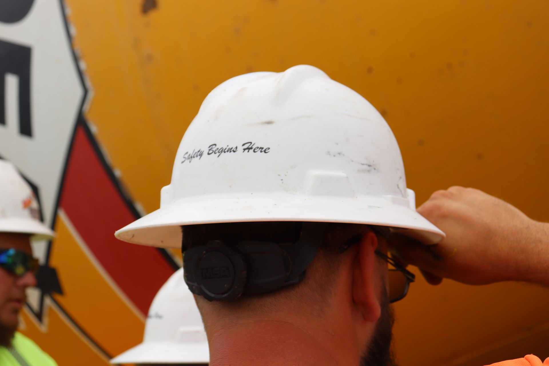 A man wearing a white hard hat that says safety begins here