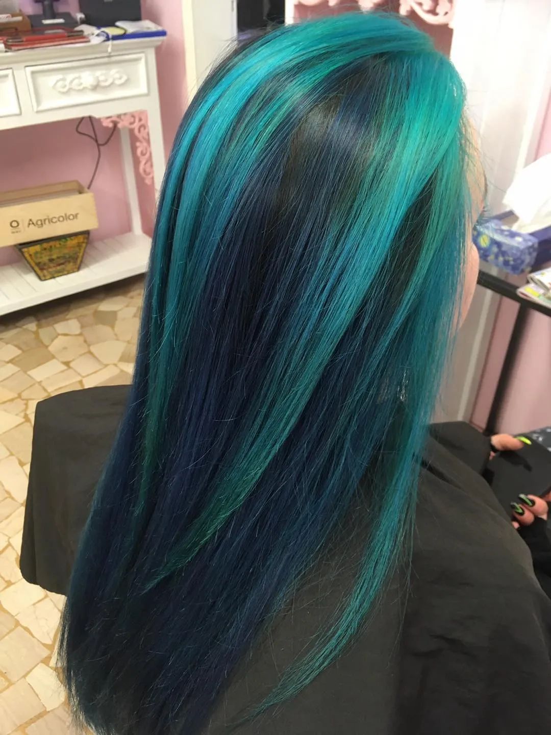 Una donna con i capelli blu e verdi è seduta su una sedia.