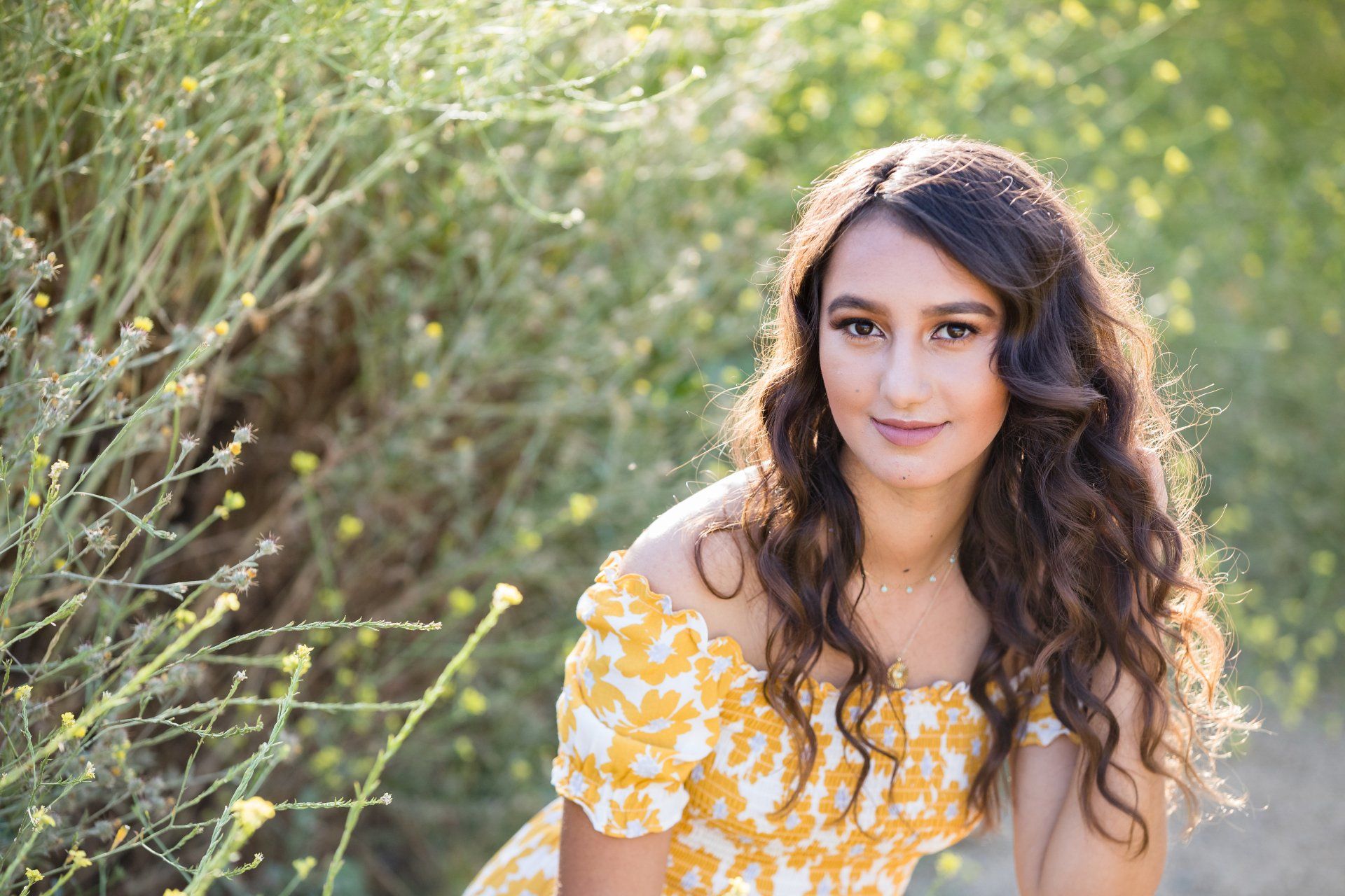 A young woman in a yellow dress is sitting in a field of flowers.