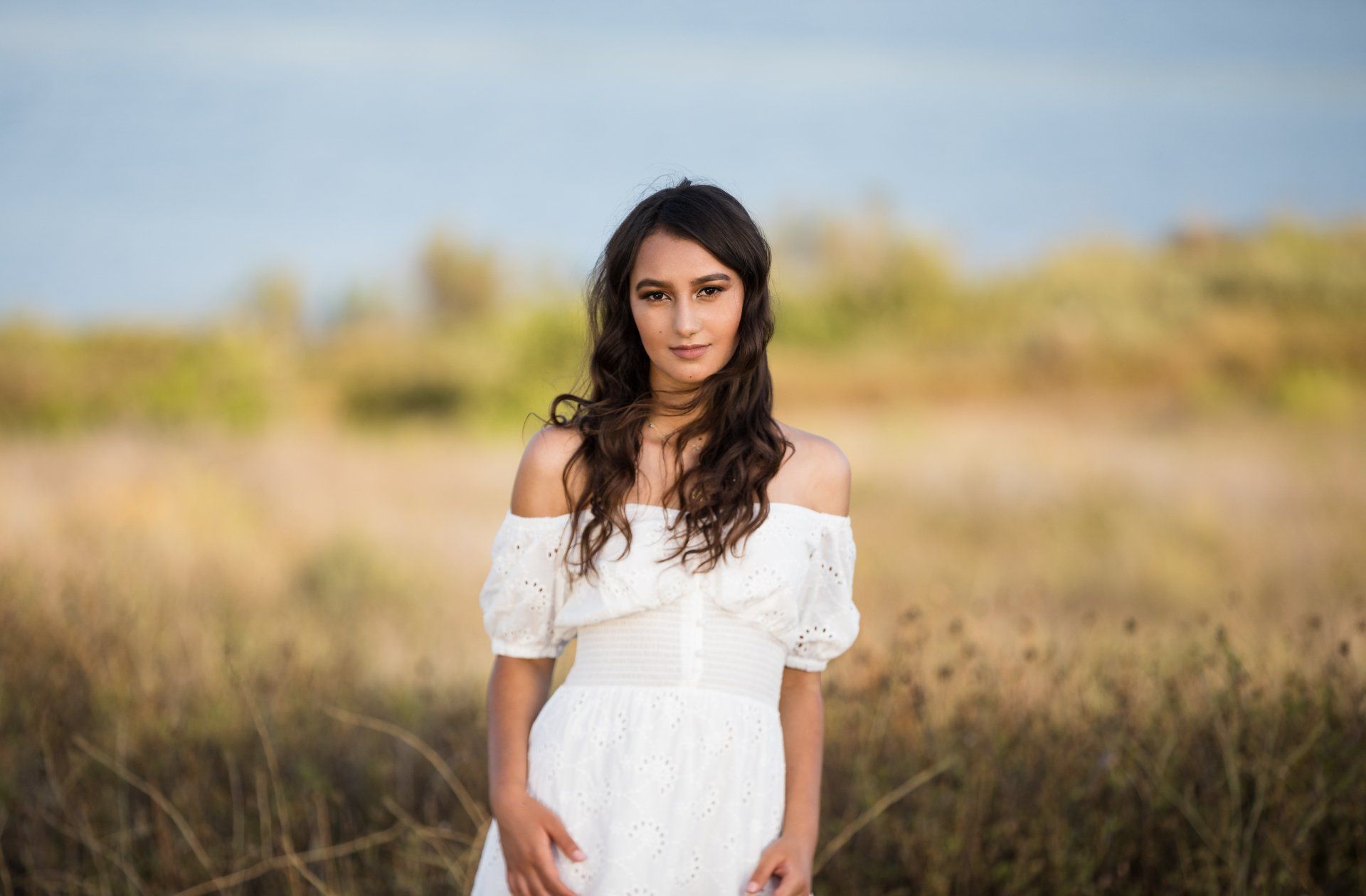 A woman in a white dress is standing in a field.
