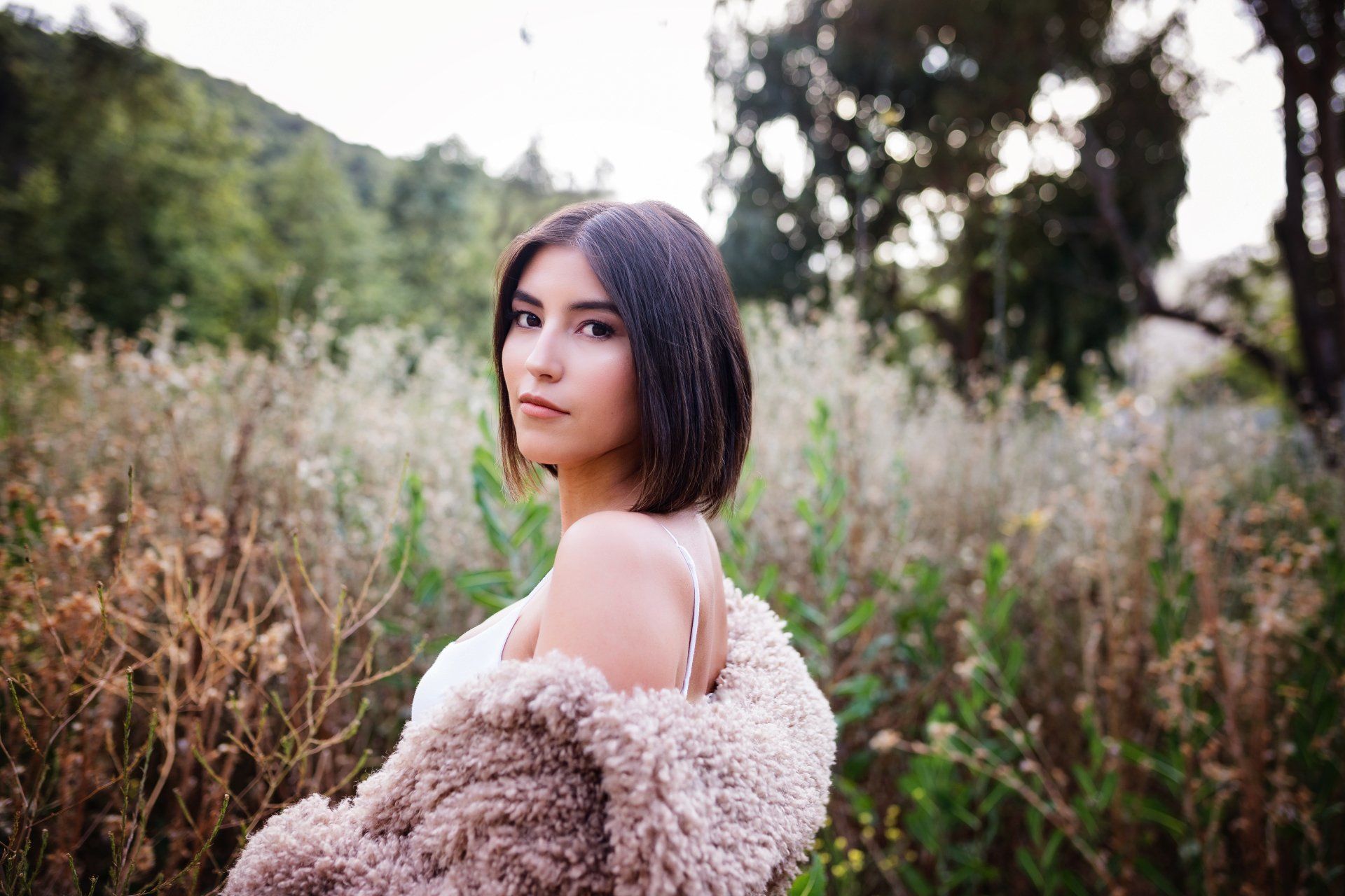 A woman in a fur coat is standing in a field.